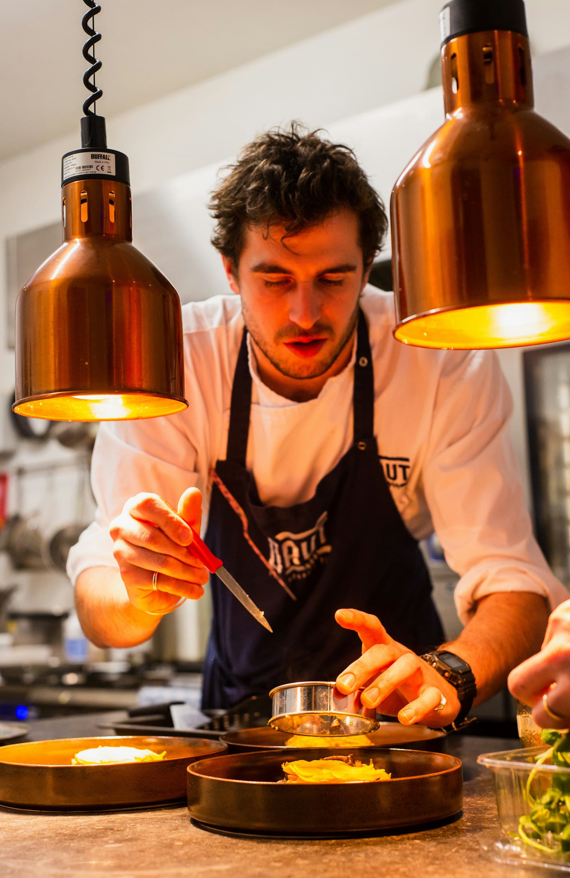 Professional restaurant chef plating at the pass under heat lamps